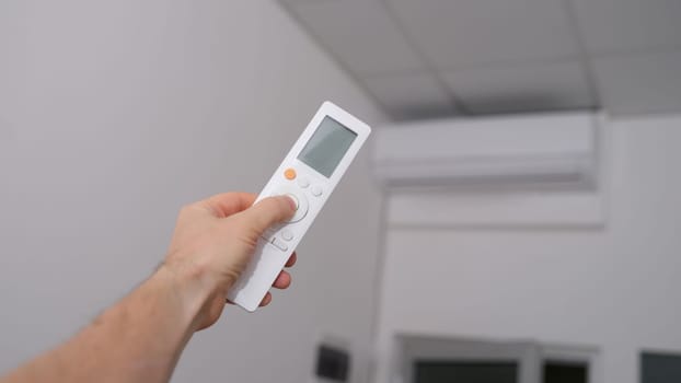 Hand with the remote control is directed to air conditioner. Climate control in office or at home concept