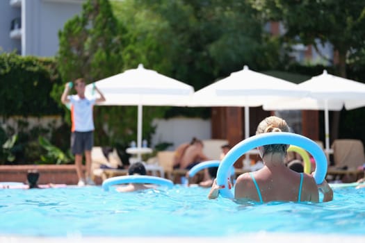 People do aqua aerobics in noodle pool. Summer sports in groups in pool