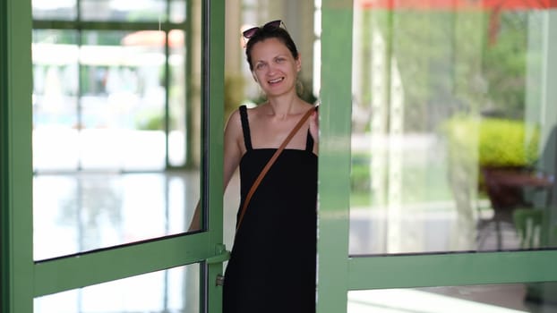 Smiling young woman opening front door to hotel house and shop. Welcome and hospitality concept