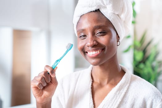 Teeth care and oral hygiene concept. Positive young Afro American woman holds toothbrush, beautiful smile, cleans teeth, has dark skin, being in high spirit. Healthcare and dentistry. High quality photo