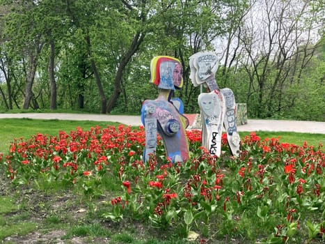 Sacral Hi-Tech Sculpture. Sculpture In the park in the form of figures of a man and a woman painted with graffiti, among flowers. Downtown. Kiev Ukraine 02-21-2023