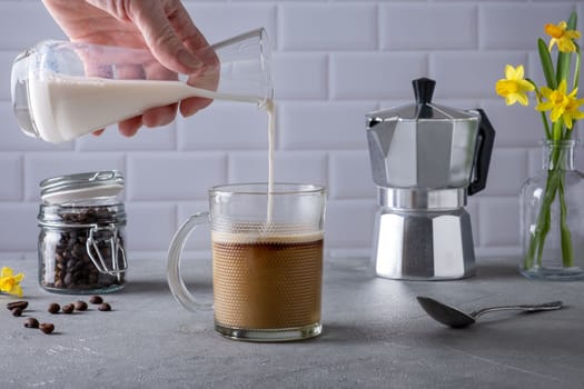 Woman's hand pours cream into glass cup with coffee. Morning traditional coffee. Selective focus