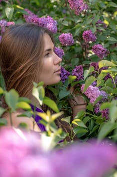 portrait of young woman with long hair outdoors in blooming lilac garden.