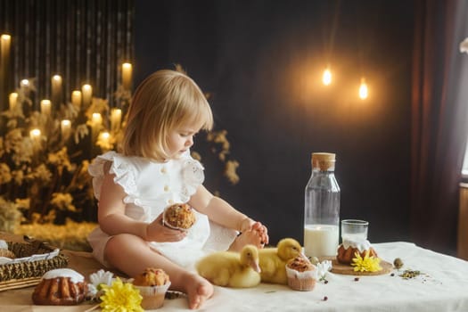 A little girl is sitting on the Easter table and playing with cute fluffy ducklings. The concept of celebrating happy Easter