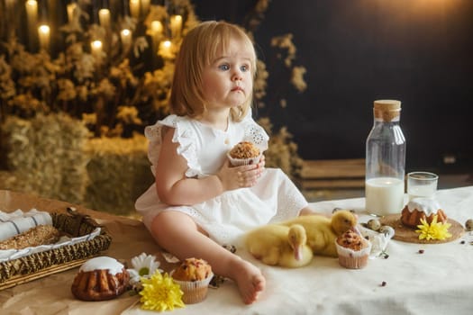 A little girl is sitting on the Easter table and playing with cute fluffy ducklings. The concept of celebrating happy Easter