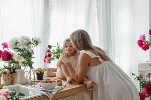 A little blonde girl with her mom on a kitchen countertop decorated with peonies. The concept of the relationship between mother and daughter. Spring atmosphere.