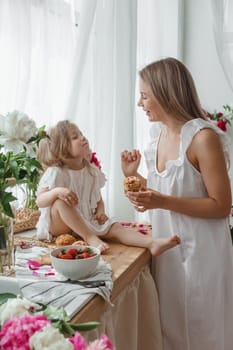 A little blonde girl with her mom on a kitchen countertop decorated with peonies. The concept of the relationship between mother and daughter. Spring atmosphere.