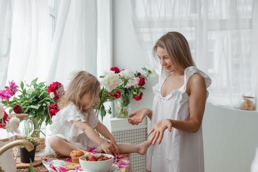 A little blonde girl with her mom on a kitchen countertop decorated with peonies. The concept of the relationship between mother and daughter. Spring atmosphere.