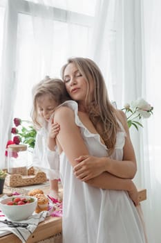 A little blonde girl with her mom on a kitchen countertop decorated with peonies. The concept of the relationship between mother and daughter. Spring atmosphere.