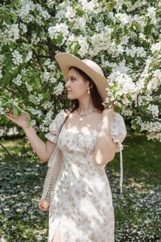 An attractive long-haired woman walks in the spring in the park of blooming apple trees. Spring portrait of a woman