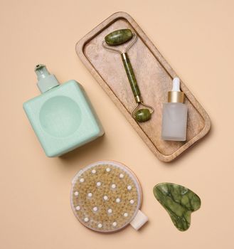 White bottle with dropper, a massage brush on a beige background, viewed from above. Cosmetic packaging