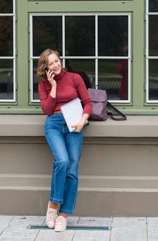 a young caucasian girl returns to college, stands with a backpack and notebooks and talks on the phone in a laugh, back to school, High quality photo