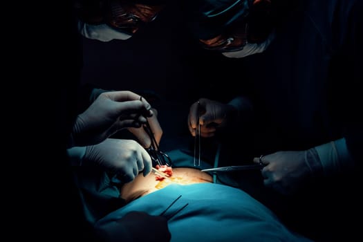 Surgical team performing surgery to patient in sterile operating room. In a surgery room lit by a lamp, a professional and confident surgical team provides medical care to an unconscious patient.