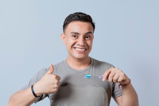 Smiling handsome guy holding a toothbrush with thumb up. Smiling people holding toothbrush with thumbs up gesture, Young man holding a toothbrush with thumb up isolated