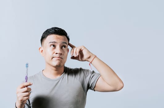 Man holding toothbrush with pensive expression isolated. Person holding toothbrush looking up, Thoughtful man holding toothbrush isolated, Portrait of young man thinking holding toothbrush