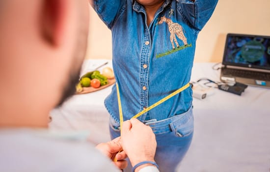 Close-up of nutritionist measuring waist to patient. View of a male nutritionist measuring female patient waist. Concept of weight loss and professional nutritionist.