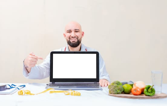 Smiling nutritionist pointing at an advertisement on the laptop, Nutritionist man pointing at laptop screen. Professional nutritionist pointing at blank laptop screen