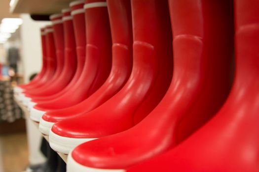 Red rubber boots of different colors on store shelves in a shop
