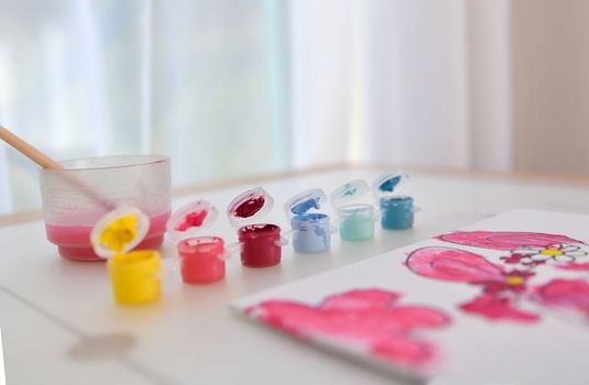 Palette with multicolor paints and water with a brush for children