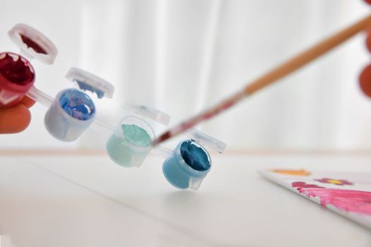 Palette with multicolor paints and water with a brush for children