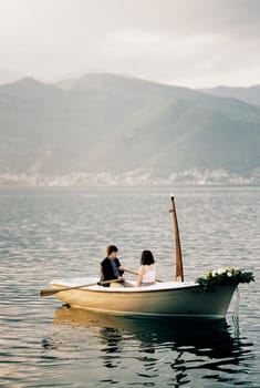 Man and woman are sailing in a boat with oars on the sea against the backdrop of mountains. High quality photo