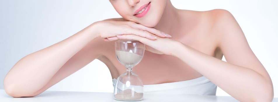 Closeup personable model holding hourglass in beauty concept of anti-aging skincare treatment. Young girl portrait with perfect smooth clean skin and flawless soft makeup in isolated background