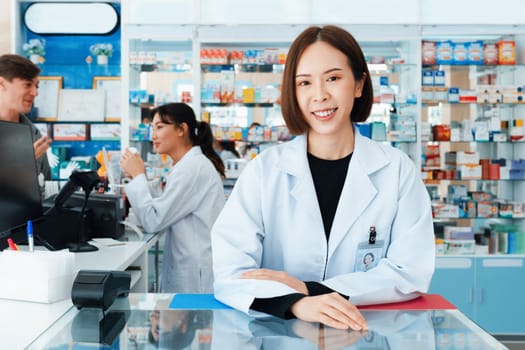 Portrait of affable asian pharmacist and qualified pharmaceutical, medicine pill bottle on shelf in background at pharmacy. Concept of pharmacist working on cashier talking to customer in drugstore.