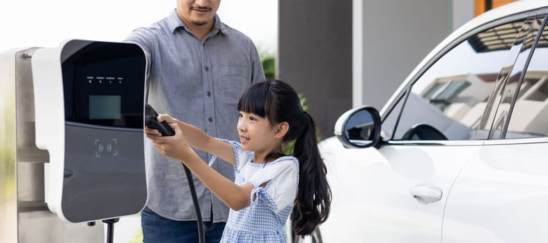 Progressive concept of a father and daughter who have just returned from school in an electric vehicle that is being charged at home. Electric vehicle driven by renewable clean energy.