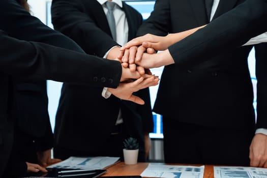 Closeup business team of suit-clad businessmen and women join hand stack together and form circle. Colleague collaborate and work together to promote harmony and teamwork concept in office workplace.