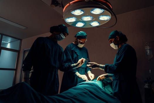 Surgical team performing surgery to patient in sterile operating room. In a surgery room lit by a lamp, a professional and confident surgical team provides medical care to an unconscious patient.