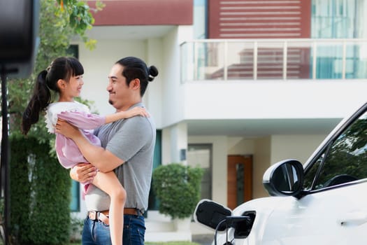 Progressive father and daughter returned from school in electric vehicle that is being charged at home. Electric vehicle driven by renewable clean energy. Home charging station concept for environment