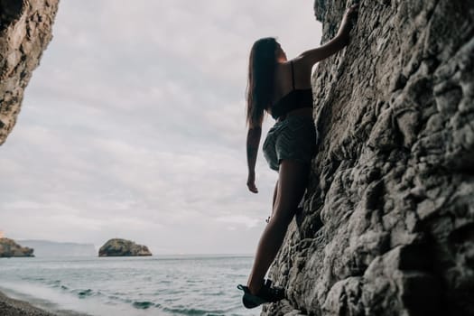 A girl climbs a rock. The athlete trains in nature. Woman overcomes difficult climbing route. Extreme hobby. Tourist woman rock climber hiking on mountains rocks over beautiful sea coast