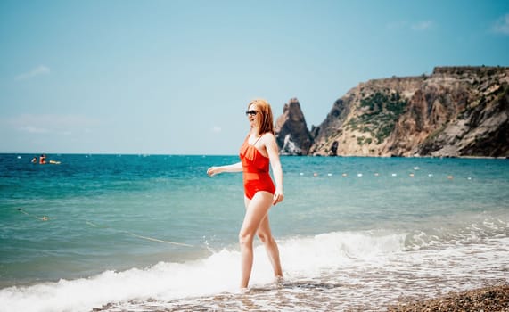 Young happy woman walks carefree on the seaside. Happy lady in red bikini. Portrait beautiful young woman relax smile around beach sea ocean in holiday vacation travel trip.