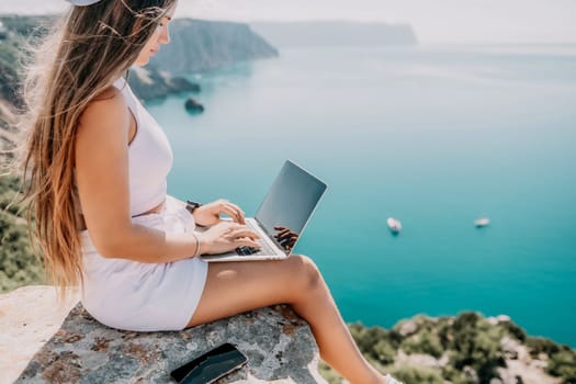 Digital nomad, Business woman working on laptop by the sea. Pretty lady typing on computer by the sea at sunset, makes a business transaction online from a distance. Freelance remote work on vacation