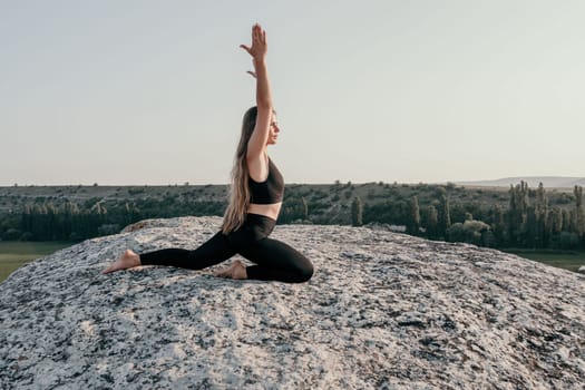 Well looking middle aged woman with long hair, fitness instructor in leggings and tops doing stretching and pilates on the rock near forest. Female fitness yoga routine concept. Healthy lifestyle.