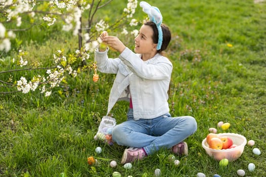 little girl wearing bunny ears with colorful Easter eggs outdoors on spring day.