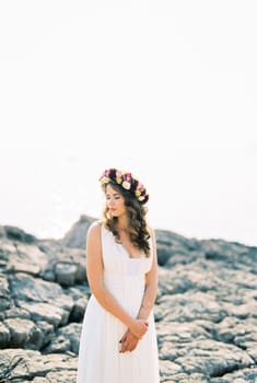 Bride in a colorful wreath stands on a rocky shore. High quality photo