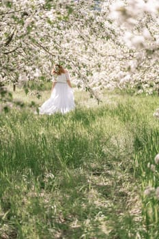 Fantasy woman in long white elegant fashion long dress walks in green spring blossom cherry garden. Happy cheerful girl princess bride. Skirt fabric flies flowing waving in wind motion