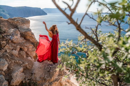 A woman in a flying red dress fluttering in the wind and a straw hat against the backdrop of the sea