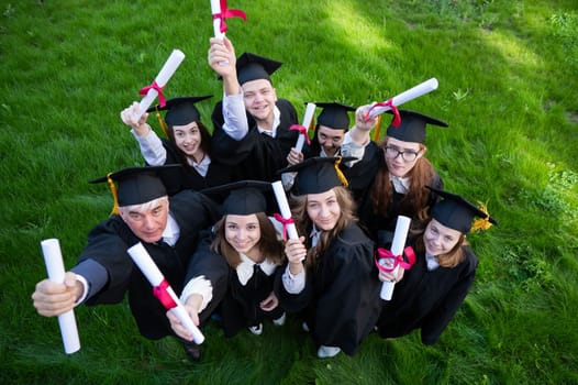 Graduates in robes show off their diplomas outdoors. View from above. Age student