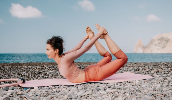 Middle aged well looking woman with black hair doing Pilates with the ring on the yoga mat near the sea on the pebble beach. Female fitness yoga concept. Healthy lifestyle, harmony and meditation.
