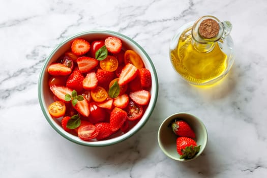 portion of strawberry and tomato cherry salad decorated with basil leaves, marble background, top view