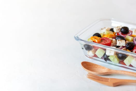 lunch box with greek salad, reusable glass container, wooden cutlery, on white background, side view, copy space