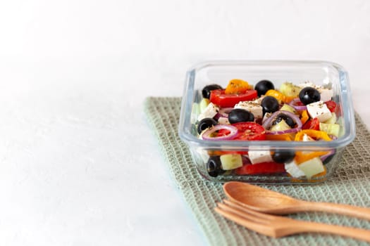 lunch box with greek salad, reusable glass container, wooden cutlery, on white background, side view, copy space