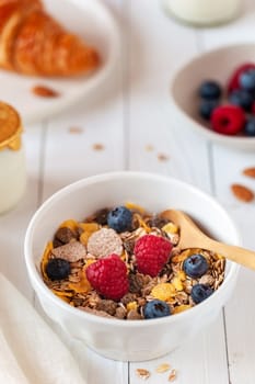 breakfast bowl of oat flakes with berries, yoghurt and croissant on the white wooden background, side view