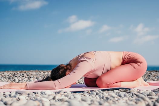 Middle aged well looking woman with black hair doing Pilates with the ring on the yoga mat near the sea on the pebble beach. Female fitness yoga concept. Healthy lifestyle, harmony and meditation.