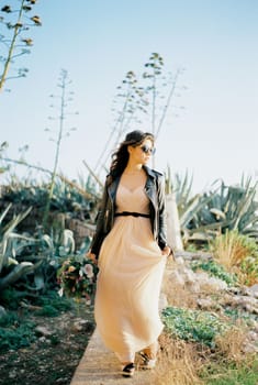 Bride in sunglasses walks along a stone curb with her head turned to the side. High quality photo