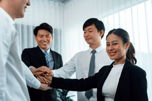 Closeup business team of suit-clad businessmen and women join hand stack together and form circle. Colleague collaborate and work together to promote harmony and teamwork concept in office workplace.