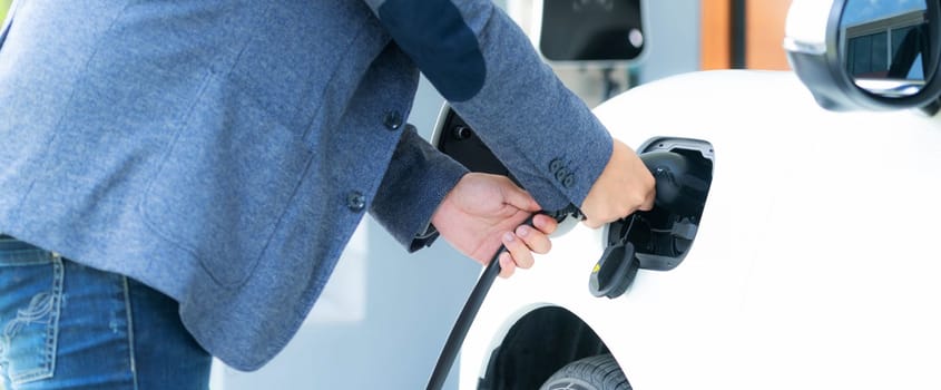 Progressive asian man install cable plug to his electric car with home charging station in the backyard. Concept use of electric vehicles in a progressive lifestyle contributes to clean environment.