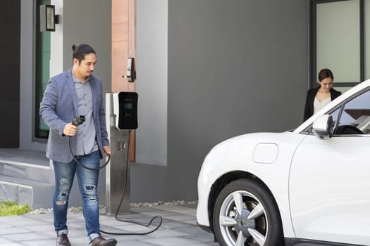 Concept of a progressive young couple with home charging station for an electric vehicle, encouraging healthy and clean environment. Electric vehicle powered by sustainable, clean energy technology.